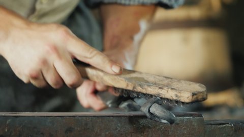 A blacksmith with a metal brush cleans the workpiece from scale and debris. Artisan craftsmanship