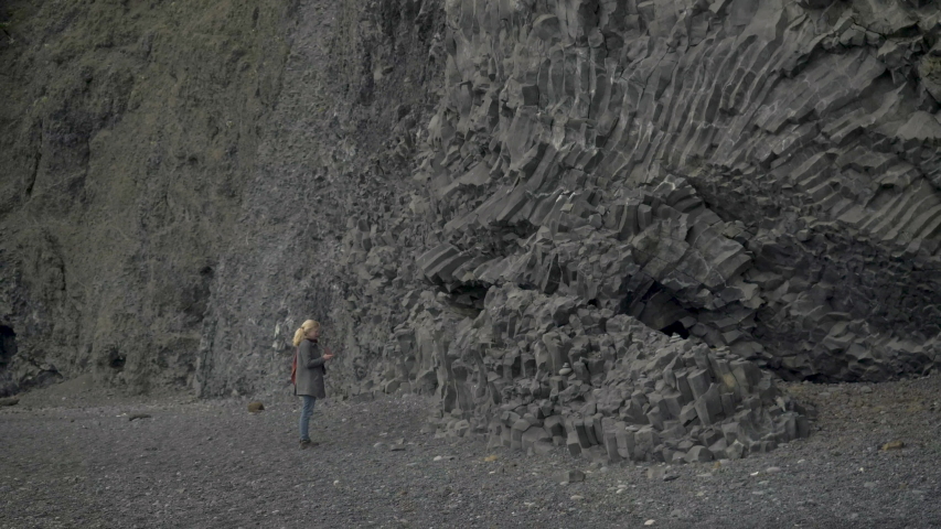 Tourist taking photos of the black volcanic rocks at Dyrhólaey. WS