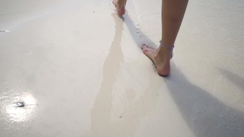 Young barefoot lady walking on white sandy beach at sunset. Legs. Body part. Maldives paradise. Travel mood. Romantic honeymoon. Super slow motion.