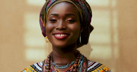 Portrait of African American young charming and happy woman in the scarf on her head and traditional look laughing to the camera. Close up face 
