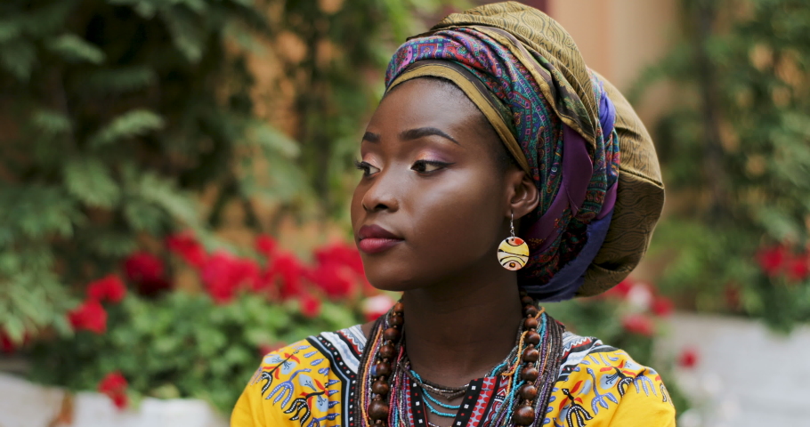 Portrait of theyoung attractive and charming African woman in the traditional outfit looking to the camera and smiling. Close up. Outside.