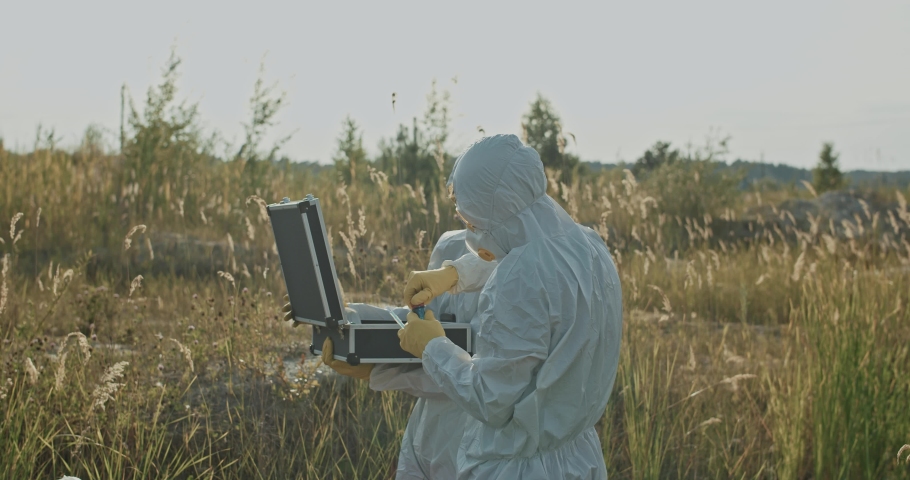 Two ecology experts eamining polluted water sample in test tube working on radioactive swamp danger area in countryside.