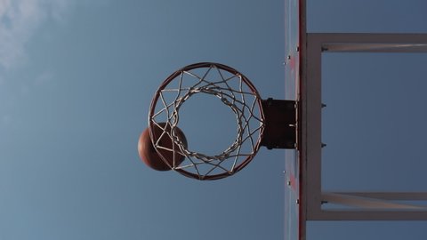Low Angle View of Ball Scoring into Basket in Slow Motion against Blue Sky Background. Healthy Lifestyle and Sport Concept.