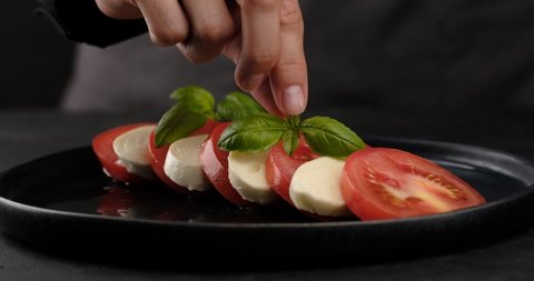 cook put basil leaf on Italian caprese salad. tomatoes, mozzarella, basil