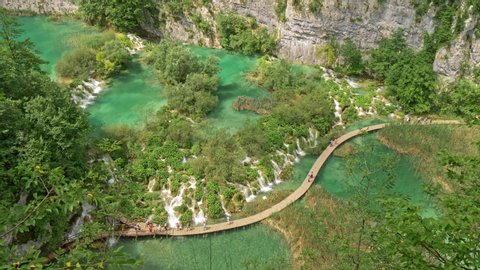 Tourists walking the boardwalk among waterfalls and cascades and green flora and turqouise lakes in Plitvice Lakes National Park, Croatia. UHD