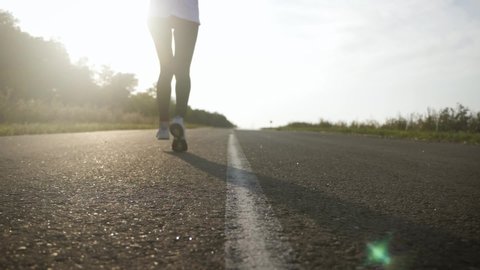 Young fitness sport woman running on road at sunset. Athlete runner feet running on road, slow motion.