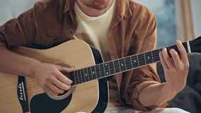 cropped view of man playing acoustic guitar on couch