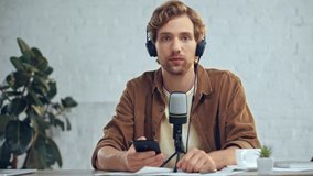 man in headphones with mic broadcasting and using smartphone