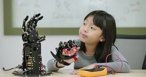 Little asian girl creates movement for mechanical robotic hand in school laboratory. Educational Technology Concept.