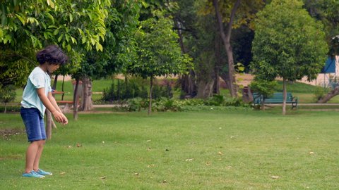 Cute Indian kid continuously doing somersaults in a park - outdoor activities to stay healthy. A young gymnastic boy showing his skills and flexibility of doing somersaults in casual wear - park vi...