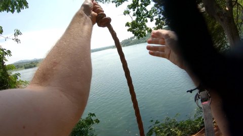 A point of view action shot of a white man swinging on a rope swing on a river bank and diving into the river Nile in Africa.