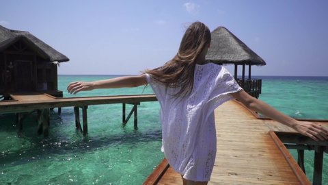Lady in white dress runs on a pier near water bungalows in the Maldives. Travel time. Romantic honeymoon. Super slow motion.