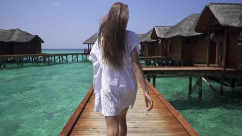 Follow me. Maldives.Young woman in white dress running and taking her man’s hand and lead to water bungalows. Fihalhohi island resort. Smiling girl, have fun. Romantic honeymoon. Super slow motion.