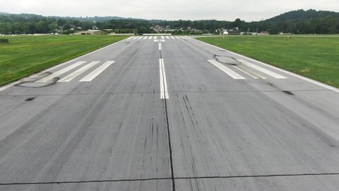 Runway threshold aerial view, flying above end of airstrip with residential area in and road in background, landing strip with marking and skid marks, pilots perspective