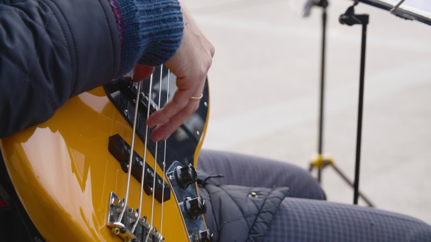 Person playing bass guitar outdoor. Close-up partial view of musician sitting on street and playing guitar. Music concept