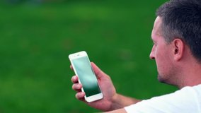 Unshaven man holding a blank mobile phone in an angled over the shoulder view of the screen outdoors with reflection