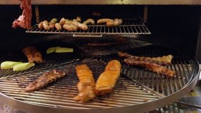 Rotating grill with portions of beef ribs , vegetables and pork sausage at a catered event panning down the machine to the paving below