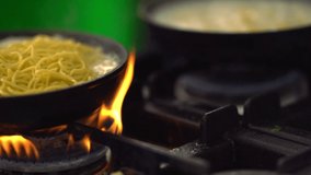 Spaghetti noodles cooking over a gas burner being removed for the addition of Italian ham and sauce while preparing a meal