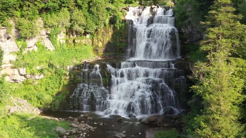 Aerial video of Chittenango Falls in Upstate New York. Flying over small wooden bridge over the river with slow pan up to large waterfall cascade.