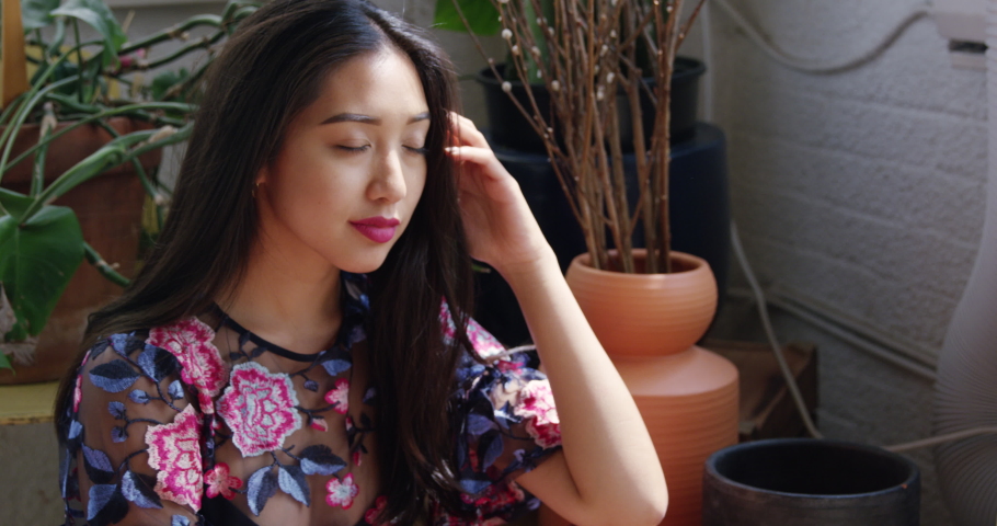 A stylish millennial woman poses for a female photographer in a bright photography studio with natural light.  Both women are glamorous and fashionable with current trends.