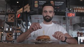 attractive young guy with a beard bites a burger sitting at a table in a cafe. man eating a burger. 4k. 4k video. 60 fps (text translation-meat,burgers,cheeseburger,additives,
minced)