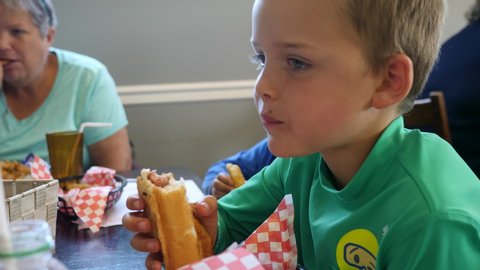 A boy eats a hot dog and french fries at a diner with his family