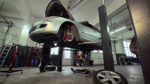The car goes down on the lift in the auto repair shop