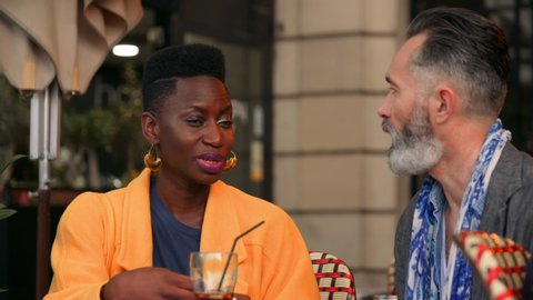 Beautiful Young Ethnic Woman Talks to her Older Boyfriend Over Dinner at an Outdoor Restaurant in France. Older Bearded Gentleman Converses with a Younger Stunning African-European Lady. 4K, slow mo.
