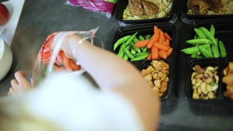 Slow Motion shot of someone doing weekly meal planning. The meals are divided by day and contain nuts, carrots, edamame, and grilled chicken on brown rice.
