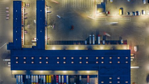 Aerial view of the large logistics park with warehouse, loading hub with many semi-trailers trucks standing at the ramps for load/unload goods at night. Hyper lapse (time lapse)