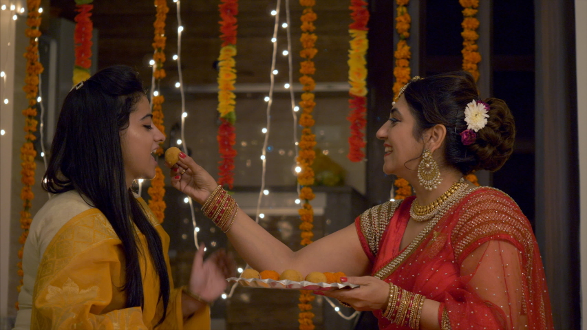 Happy Indian Family in colorful dress during Festive Season - Mother teasing and feeding ladoo to her daughter.
