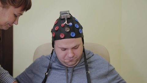 The doctor puts on a man a headset for the study of the human brain.
