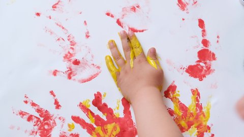A little girl stained her hands and clothes in paint while drawing. The child carefully examines the dirty hands.