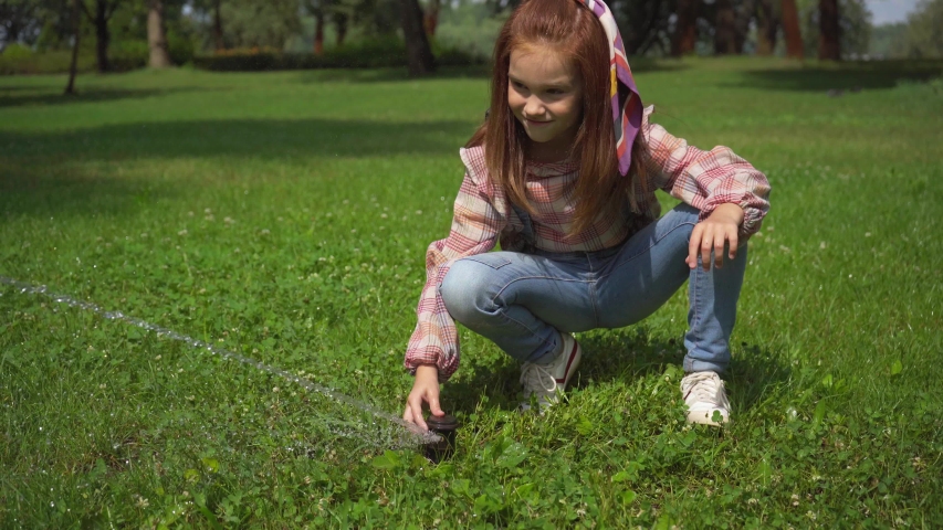 happy child playing with water stream on green grass