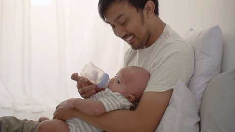 portrait of father giving a bottle of milk to his newborn baby