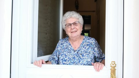 elderly senior woman opening front door of her house and welcoming people at home 