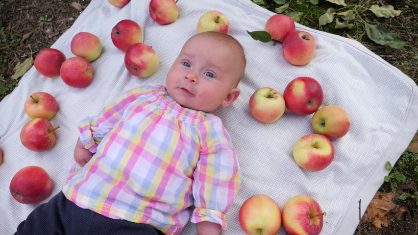 Infant baby child lie on a rug in garden with apples fruits decoration around