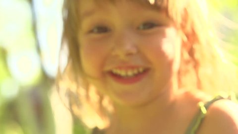 Portrait of a smiling little girl close up. Cute three years old child enjoying nature outdoors. Healthy carefree kid playing outside in summer park. Full HD 1080p. High speed camera, slow motion 