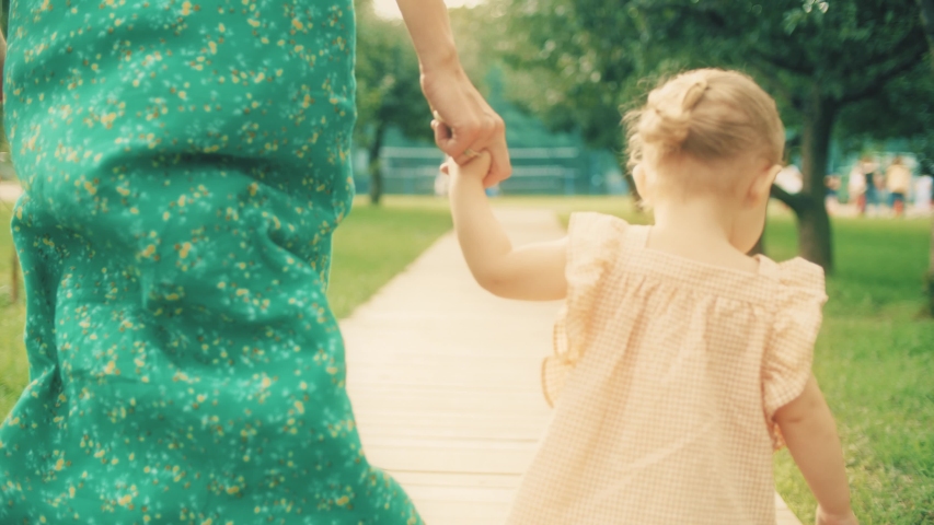 Little baby girl and her mom walk together in the park on a summer day