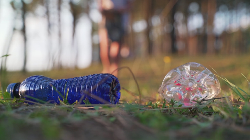 Anonymous volunteer picking litter in forest. Unrecognizable person coming close to camera then picking plastic bottles from ground and putting garbage in bag Royalty-Free Stock Footage #1036959134