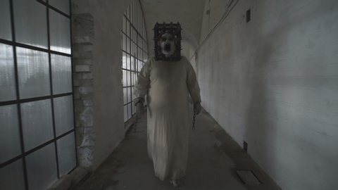A scary ghost of a fat woman with a rusty cage on her head and with shackles on her hands wanders through gloomy corridors of an abandoned psychiatric hospital. 4K