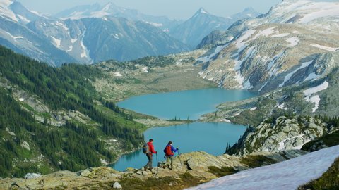 Young adventurous male female Heli hikers Caucasian tourists viewing glacial mountain lake in summer Canada British Columbia RED MONSTRO