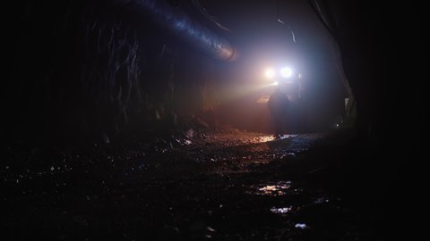 Silhouette of a worker with headlamp walking through a mine dark tunnel, lit by lights of mining machinery.
