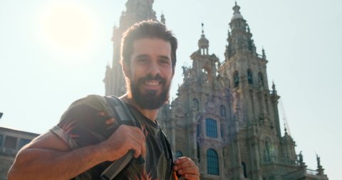 Portrait of happy male pilgrim looking at camera in Santiago de Compostela, Spanish town at the end of Camino de Santiago or Way of St James. Young man smiling in Spain, slow motion
