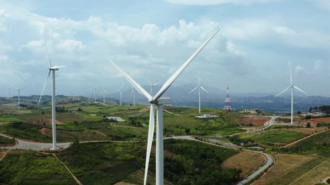 Aerial view, windmills rotating by the force of the wind and generating clean renewable energy for sustainable development in green ecologic way on cloudy sky at highland. Panorama curve shot by drone