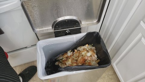 Home cooking - High angle view of peeling onion using utility knife and collecting scraps into stainless steel compost bin with black garbage bag.