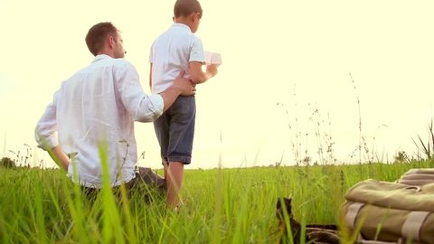 Happy Father and Son playing with paper airplane on the field. Kid throws a paper plane, dream, freedom concept. Dad with Little Boy enjoying nature together. Free, freedom concept. Slow motion 240fps