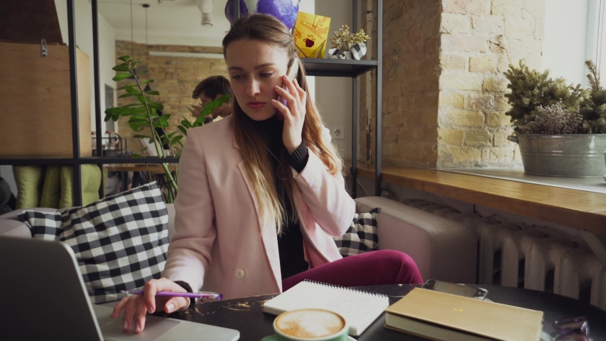 Happy Businesswoman Talking On The Phone. Woman In Cafe, use mobile Phone, Working On Notebook. Lady at cafeteria using phone and laptop, drink cup coffee. Pretty Businesswoman Working On Her Break. | Shutterstock HD Video #1036994504