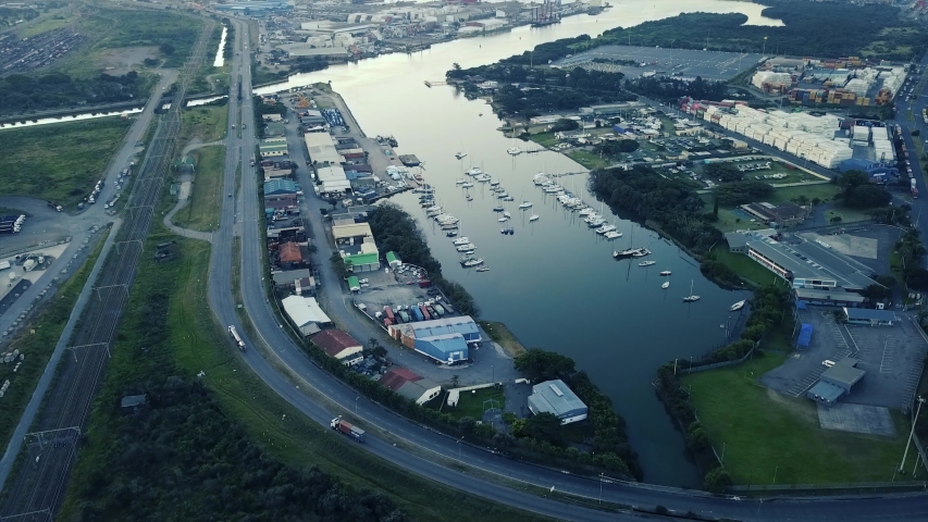 footage of sunset overlooking yachts moored with traffic on a road and shipping containers to be transported to ships by trucks.Train tracks in the distance. Bluff Yacht club Durban Harbour.
