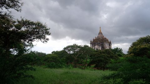 distant view of Thatbyinnyu Temple under cloudy sky. The highest pahto in Bagan Myanmar. Forest and grass field foreground 